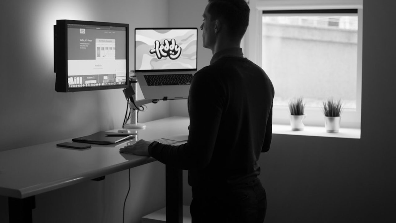 a man standing next to his dual-monitor desk