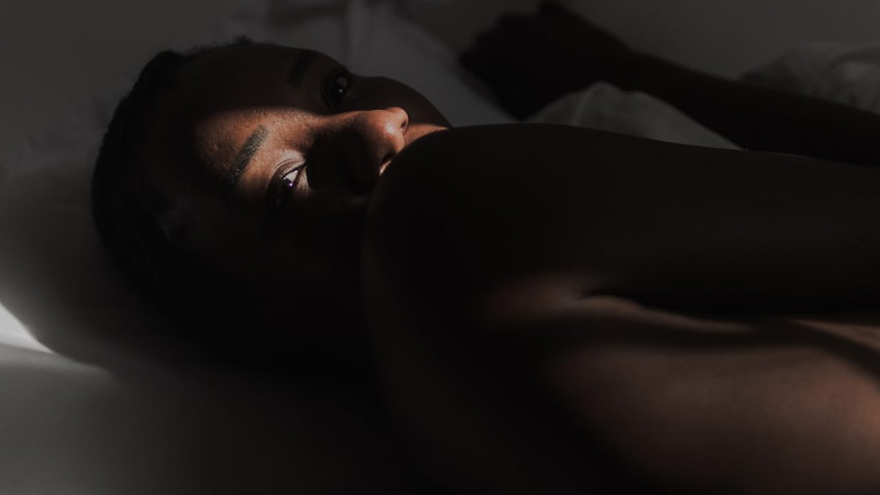 An African woman is lying on a bed as light falls on her face