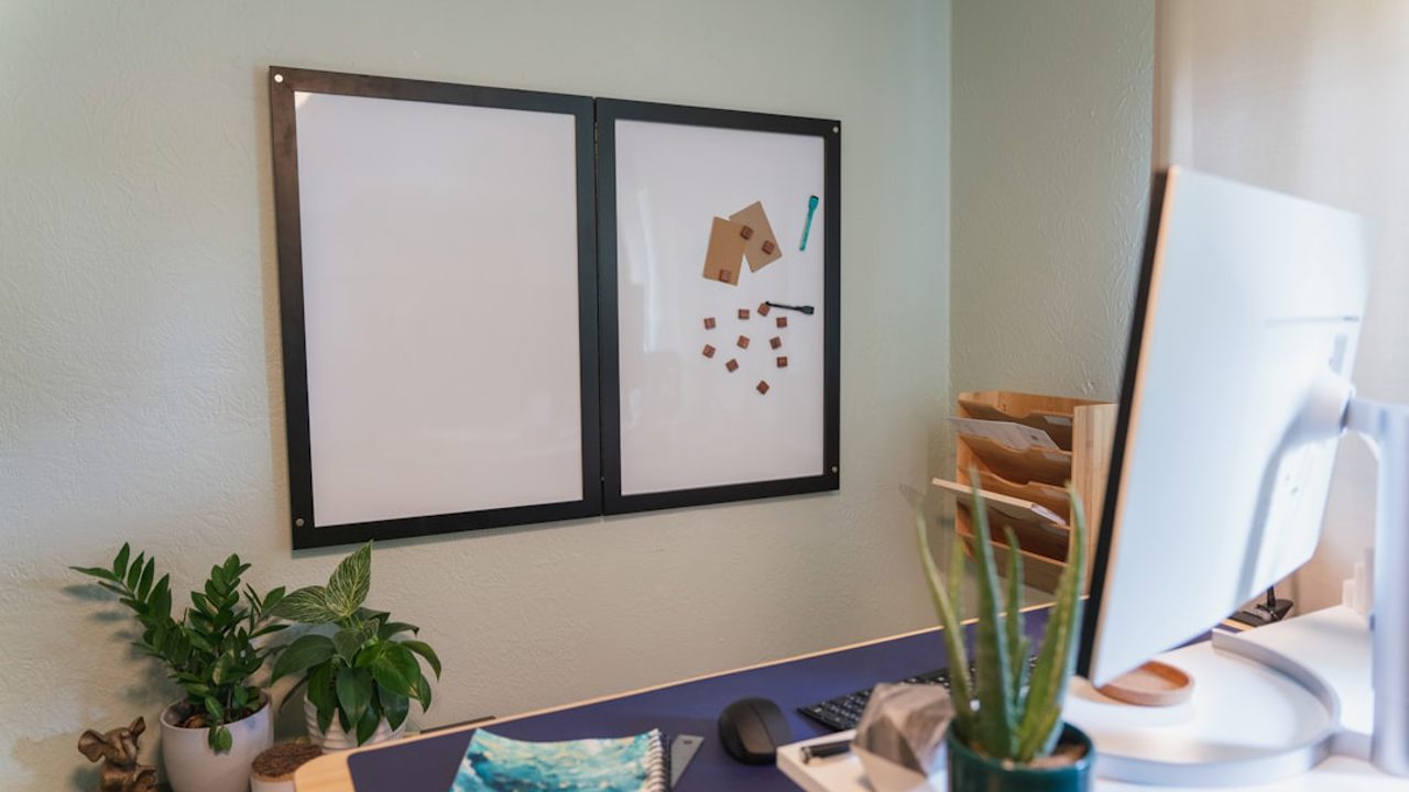 Optimieren Sie Ihr Homeoffice-Erlebnis mit einem sorgfältig eingerichteten Schreibtisch, der Pflanzen, ein Notizbuch und ein an der Wand befestigtes Whiteboard umfasst, das die Produktivität steigert.