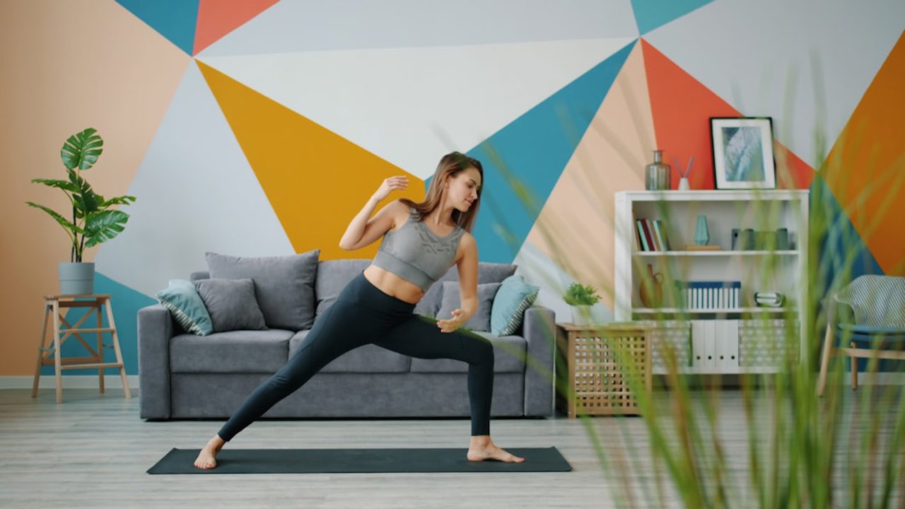 A beautiful girl is doing yoga exercises on the floor at home, stretching her body and focusing on the practice. Youth, indoor, and healthy lifestyle concept.